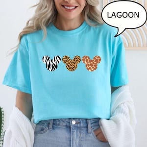 Pu&ograve; includere: Una maglietta azzurra con tre sagome della testa di Topolino con motivi animalier: zebra, leopardo e giraffa. La parola "LAGOON" &egrave; in un fumetto nell'angolo in alto a destra.