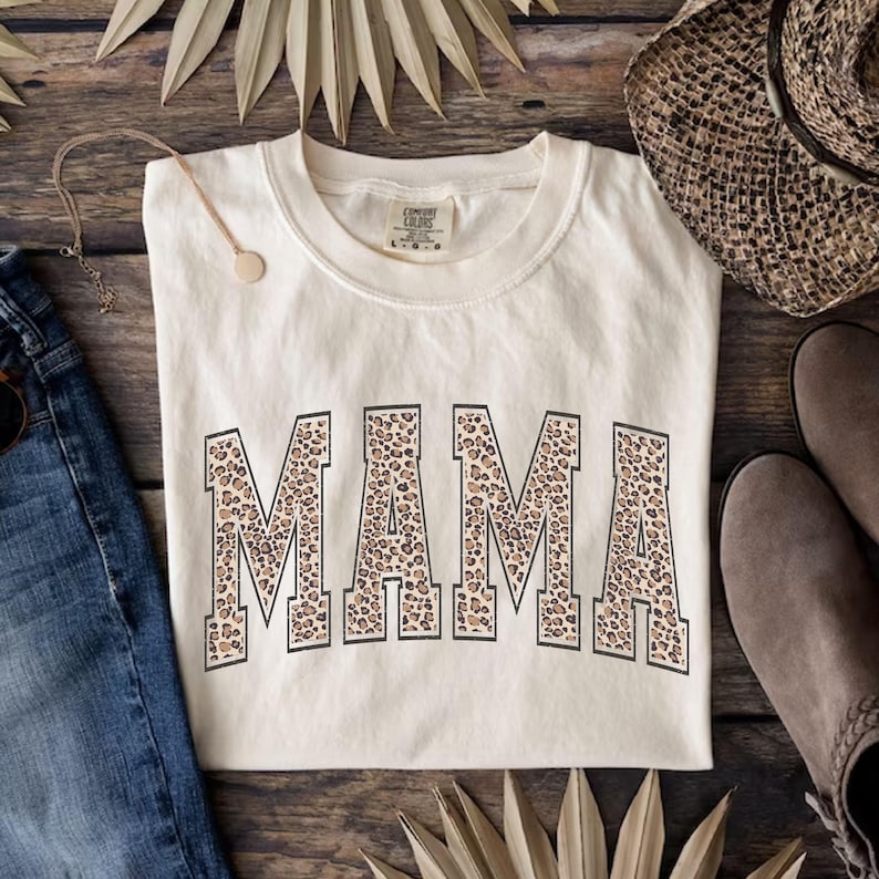 May include: A cream colored t-shirt with a leopard print "MAMA" graphic.