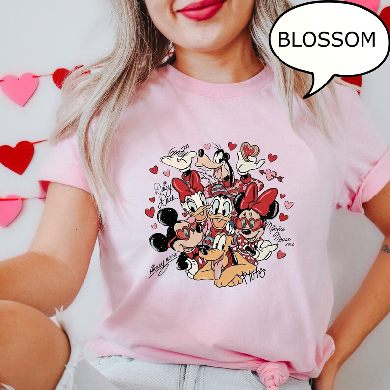 May include: Pale pink t-shirt with a Disney character graphic including Mickey and Minnie Mouse, Donald and Daisy Duck, Goofy, and Pluto, with hearts. The shirt has rolled sleeves and a speech bubble with the word "BLOSSOM".