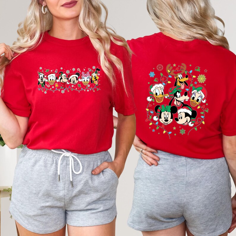 May include: Red t-shirt featuring a festive design with Disney characters. The front of the shirt displays a line of characters, while the back showcases a circular arrangement of characters, all adorned with holiday elements like Santa hats and lights.