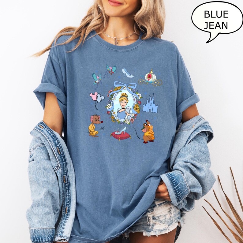 May include: A blue jean t-shirt with a graphic print of Cinderella, her mice friends, and other elements from the Disney movie Cinderella. The graphic includes a glass slipper, a castle, and a carriage.