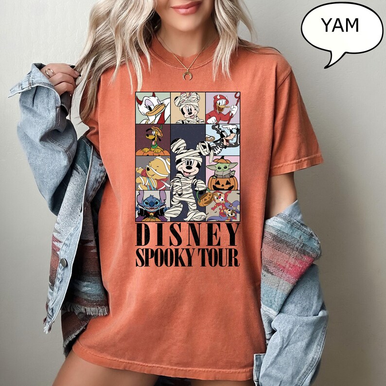 May include: Orange t-shirt featuring a colorful graphic of Disney characters in Halloween costumes. The design includes Donald Duck, Mickey Mouse, and Stitch. The text "DISNEY SPOOKY TOUR" is printed below the characters.