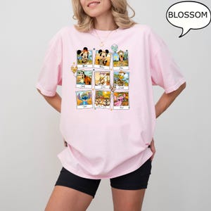Puede incluir: Camiseta rosa con un gr&aacute;fico de nueve personajes de Disney en marcos de fotos. Los personajes incluyen a Mickey Mouse, Pluto, Donald Duck, Stitch y Chip y Dale. El texto "Blossom" est&aacute; en un bocadillo de di&aacute;logo en la esquina superior derecha de la imagen.