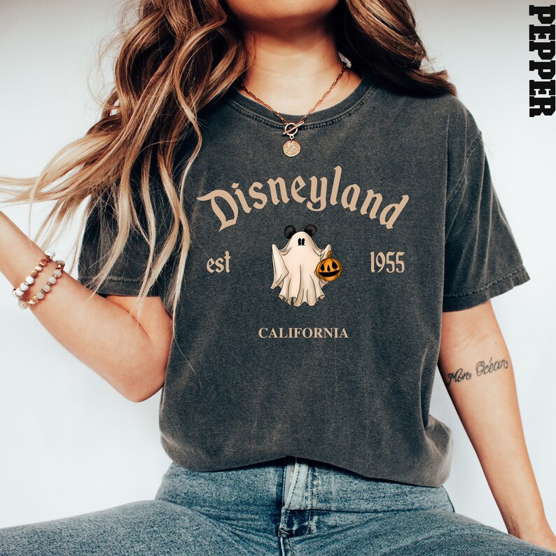 Puede incluir: Una camiseta gris oscuro con un gr&aacute;fico de estilo vintage de un fantasma sosteniendo una calabaza. El texto "Disneyland est 1955 California" est&aacute; impreso en la camiseta.
