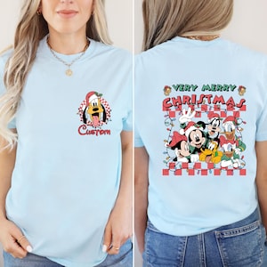 May include: Light blue t-shirt featuring a cartoon image of Pluto wearing a Santa hat with the word "Custom" below. The back of the shirt displays a group of Disney characters with the words "Very Merry Christmas".