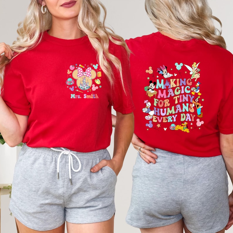 May include: Red t-shirt with a colourful graphic on the front featuring a castle, Minnie Mouse ears, and the text "Mrs. Smith." The back of the shirt has the text "MAKING MAGIC FOR TINY HUMANS EVERY DAY" with cartoon characters.