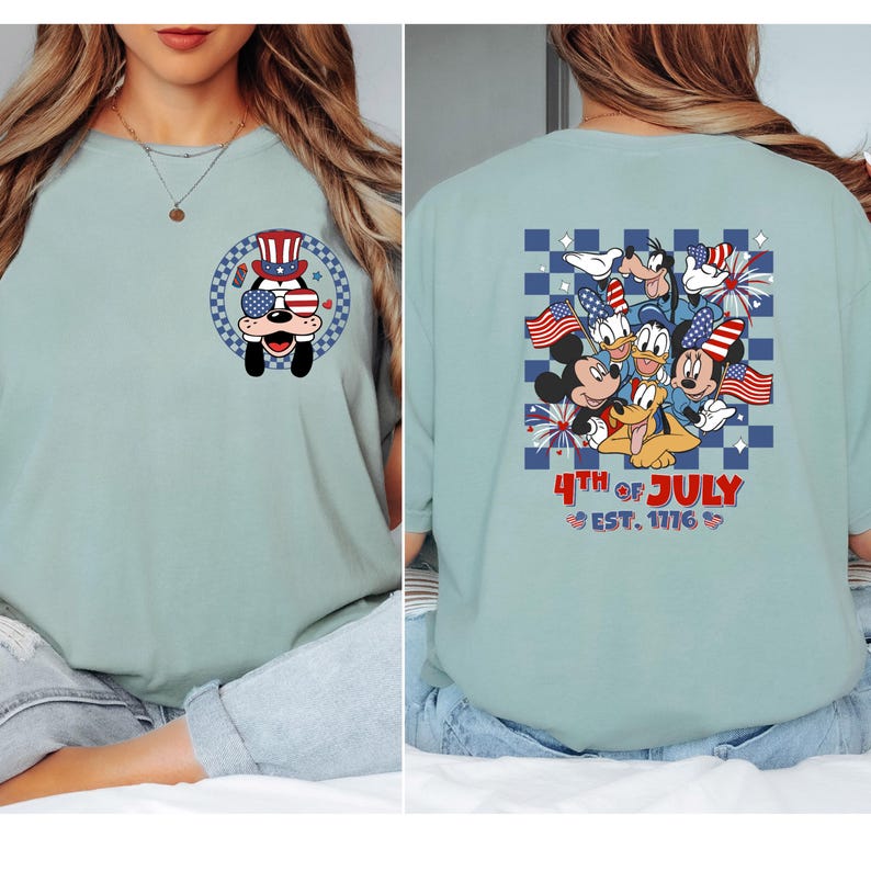 Pode incluir: Camiseta azul claro com um cachorro de desenho animado usando &oacute;culos de sol e chap&eacute;u patri&oacute;ticos. A parte de tr&aacute;s da camisa mostra personagens de desenho animado com bandeiras americanas e fogos de artif&iacute;cio, com o texto "4th of July Est. 1776."