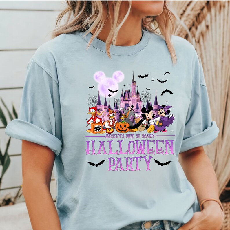 May include: Light blue t-shirt with a purple graphic of Mickey Mouse and friends in front of the Disney castle. The graphic includes bats, spiderwebs, and the text "Mickey's Not So Scary Halloween Party".