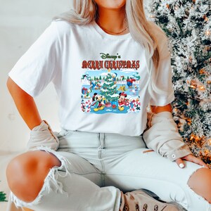 May include: White t-shirt with a colorful graphic of Mickey Mouse and friends celebrating Christmas. The text "Disney's Merry Christmas" is printed above the graphic.