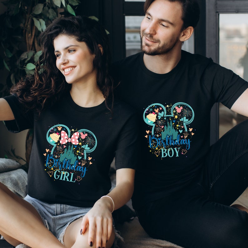 Puede incluir: Dos camisetas negras con un estampado gr&aacute;fico de un castillo, fuegos artificiales y orejas de Mickey Mouse. El texto en las camisetas dice "Birthday Girl" y "Birthday Boy".