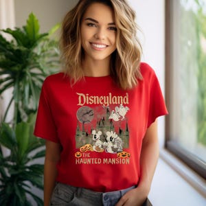 May include: Red t-shirt with a vintage-style graphic of Disneyland's Haunted Mansion. The graphic features Mickey Mouse and ghosts in front of the Haunted Mansion, with the text "Disneyland" and "The Haunted Mansion" above and below the image.