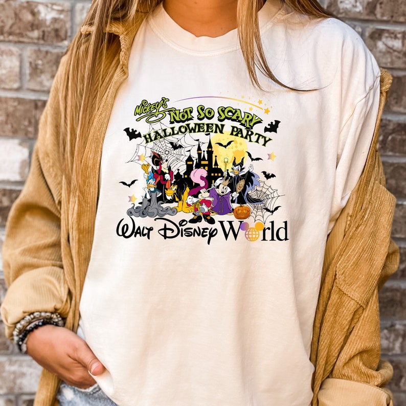 May include: White t-shirt with a colorful graphic of Mickey's Not So Scary Halloween Party at Walt Disney World. The graphic features Mickey Mouse, Minnie Mouse, Goofy, Donald Duck, and other Disney characters in Halloween costumes.