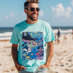 May include: A light blue t-shirt with a distressed graphic print of Buzz Lightyear from the Toy Story franchise. The graphic features Buzz Lightyear flying in space with other characters from the movie. The text "Buzz Lightyear Laser Blast" is printed on the graphic.