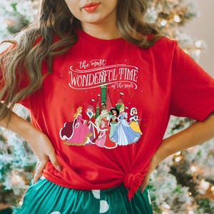 May include: Red t-shirt with a white graphic of Disney princesses in front of a castle with the text "the most WONDERFUL TIME of the year".