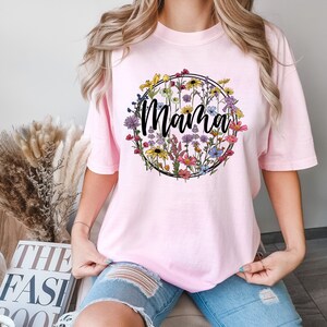 Peut inclure: T-shirt rose avec un motif de couronne de fleurs et le mot "Mama" en lettres noires.