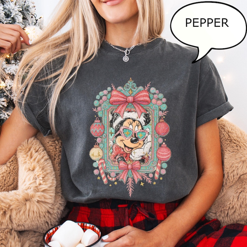 Puede incluir: Camiseta gris oscuro con un dise&ntilde;o festivo de Minnie Mouse con gafas de sol y gorro de Pap&aacute; Noel, rodeada de adornos navide&ntilde;os y bastones de caramelo. La palabra "PEPPER" est&aacute; en una burbuja.