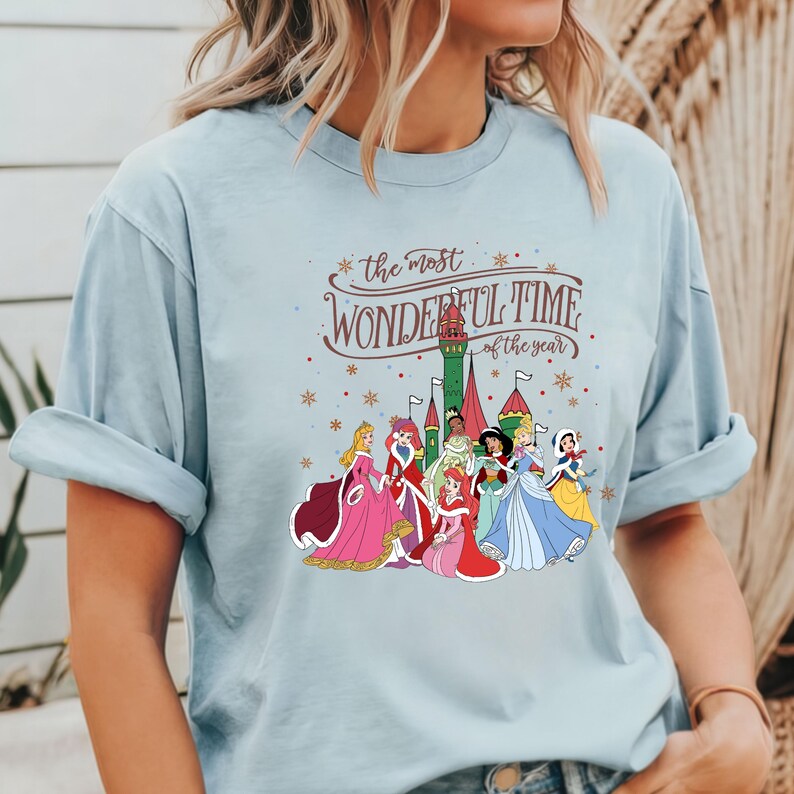 May include: Light blue t-shirt with a graphic of Disney princesses in front of a castle. The text "the most wonderful time of the year" is printed on the shirt.