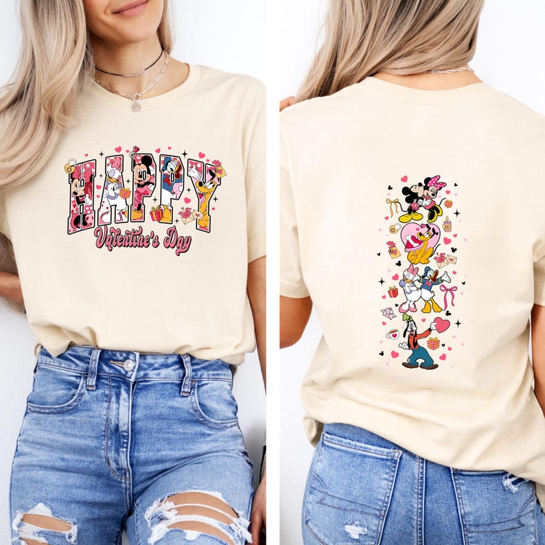 May include: Beige t-shirt with a Valentine's Day design. The front features the word "HAPPY" with Disney characters and the text "Valentine's Day." The back displays a vertical arrangement of Disney characters. The shirt is paired with blue jeans.