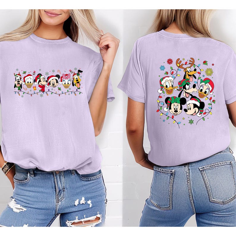 May include: A light purple t-shirt featuring a festive design with Disney characters, including Mickey Mouse, Donald Duck, and Goofy, wearing Christmas hats and surrounded by string lights. The back of the shirt also has a similar design.
