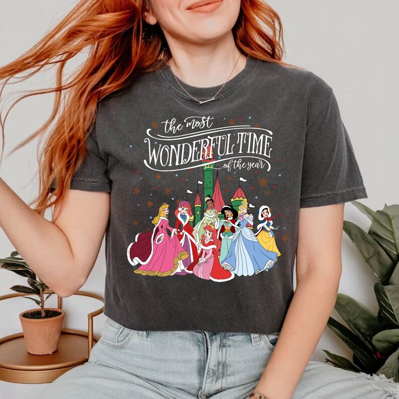 May include: A dark gray cropped t-shirt with a white graphic print of Disney princesses in front of a castle. The text "the most wonderful time of the year" is printed above the princesses.