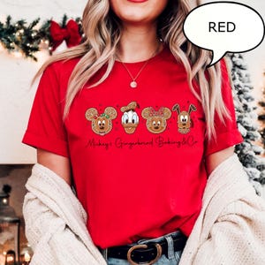 Puede incluir: Una camiseta roja con dise&ntilde;os de galletas de jengibre de Mickey Mouse, el Pato Donald, Minnie Mouse y Pluto. El texto "Mickey's Gingerbread Baking & Co" est&aacute; impreso debajo de los personajes. Una burbuja de di&aacute;logo con la palabra "RED" est&aacute; en la esquina superior derecha.