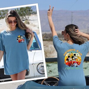 以下が含まれることがあります： ミッキーマウスとその仲間たちのグラフィックがプリントされた青いTシャツを着た女性2人。シャツの後ろには「Nothing Can Stop Us Now」という文字が書かれている。