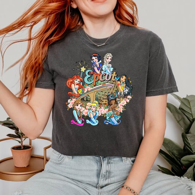 May include: A dark grey cropped t-shirt featuring a vintage-inspired graphic of Disney princesses at Epcot. The graphic depicts Snow White, Cinderella, Ariel, Belle, Tiana, and Mulan.