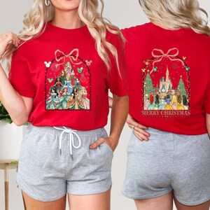 May include: Red t-shirts with a Christmas design. The front shows cartoon princesses in an arch. The back features a castle and the words "MERRY CHRISTMAS". The shirts are short-sleeved.