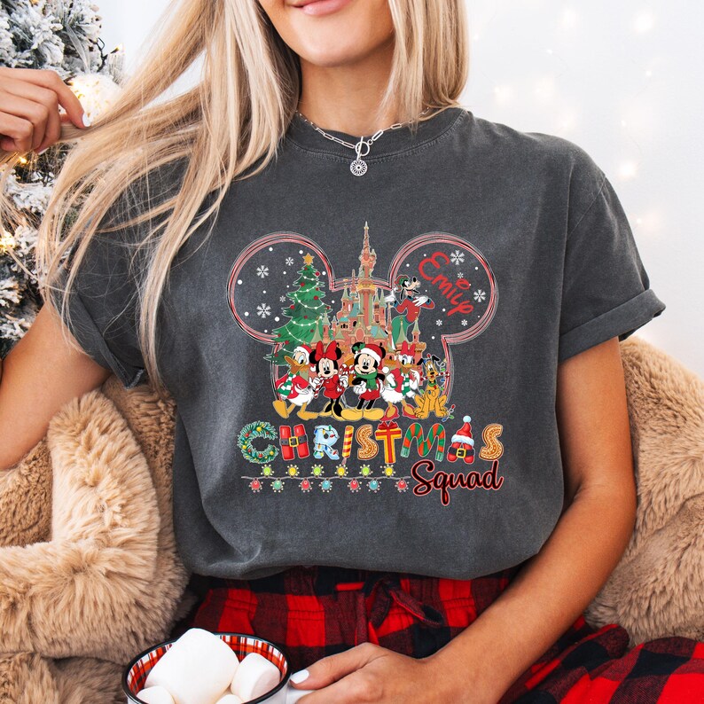 May include: Dark gray t-shirt featuring a colorful graphic of Disney characters in front of a castle and Christmas tree. The text "Christmas Squad" is below the graphic, with the name "Emily" above the graphic.