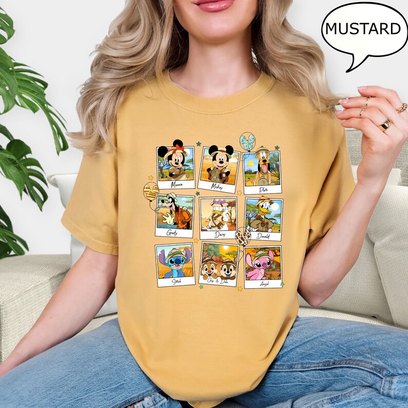 Puede incluir: Una camiseta amarilla mostaza con un estampado gr&aacute;fico de personajes de Disney con atuendos de safari. Los personajes incluyen a Mickey Mouse, Minnie Mouse, Pluto, Goofy, Donald Duck, Daisy Duck, Stitch, Chip y Dale. El texto "MUSTARD" est&aacute; en un bocadillo de di&aacute;logo en la esquina superior derecha de la imagen.