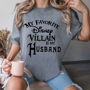 Pu&ograve; includere: Maglietta grigia con testo nero che dice "Il mio cattivo Disney preferito &egrave; mio marito".