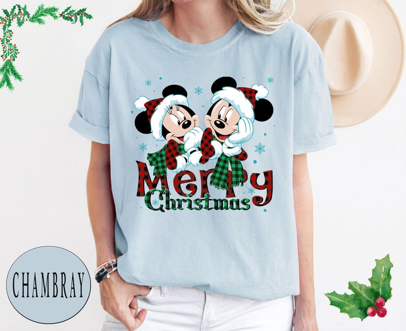 May include: Light blue t-shirt with a Christmas-themed design featuring Mickey Mouse and Minnie Mouse wearing Santa hats and scarves. The text "Merry Christmas" is printed below the characters.