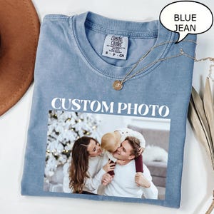 May include: A blue jean-colored t-shirt with the words "CUSTOM PHOTO" printed in white. The shirt features a family photo and a gold necklace. A speech bubble says "BLUE JEAN".