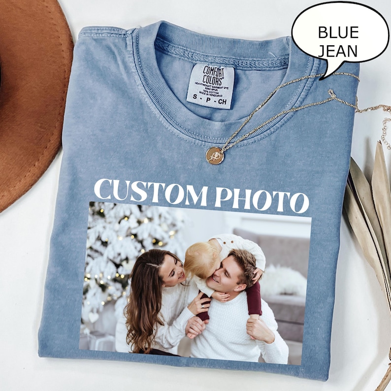 May include: A blue jean-colored t-shirt with the words "CUSTOM PHOTO" printed in white. The shirt features a family photo and a gold necklace. A speech bubble says "BLUE JEAN".