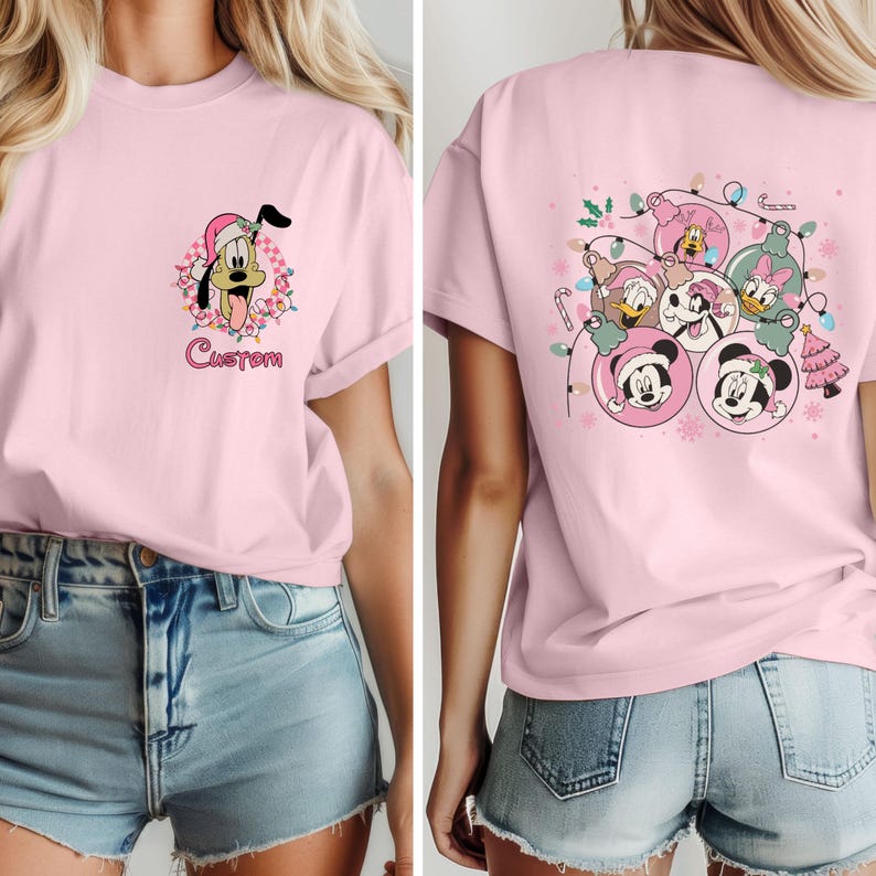 K&ouml;nnte beinhalten: Hellrosa T-Shirt mit einem Cartoon von Pluto mit Weihnachtsm&uuml;tze und Lichterketten, darunter das Wort "Custom". Auf der R&uuml;ckseite des Shirts sind Mickey, Minnie, Donald und Daisy in Weihnachtskugeln abgebildet.
