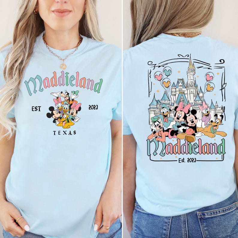 K&ouml;nnte beinhalten: Hellblaues T-Shirt mit einem Aufdruck von Mickey Mouse und seinen Freunden vor einem Schloss. Der Text "Maddieland Est. 2023" ist auf dem Shirt gedruckt.