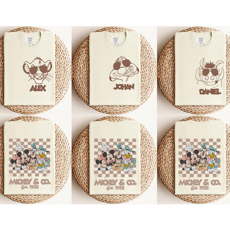 May include: Cream-colored t-shirts featuring cartoon characters with sunglasses. The shirts display characters like Simba, Timon, and Pumbaa, along with names. Other shirts showcase Mickey Mouse, Donald Duck, and Goofy with the text "MICKEY & CO. Est. 1928."