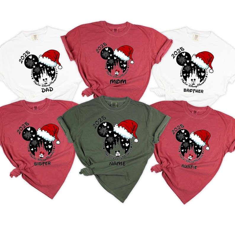 Peut inclure: Six t-shirts rouges, blancs et verts avec une silhouette noire et blanche de Mickey Mouse portant un bonnet de P&egrave;re No&euml;l. La silhouette est devant une image noire et blanche du ch&acirc;teau de Cendrillon avec des feux d'artifice. Le texte "2025" est au-dessus de la silhouette. Chaque t-shirt a un mot diff&eacute;rent sous la silhouette : "Papa", "Maman", "Fr&egrave;re", "S&oelig;ur", "Nom" et "Tante".