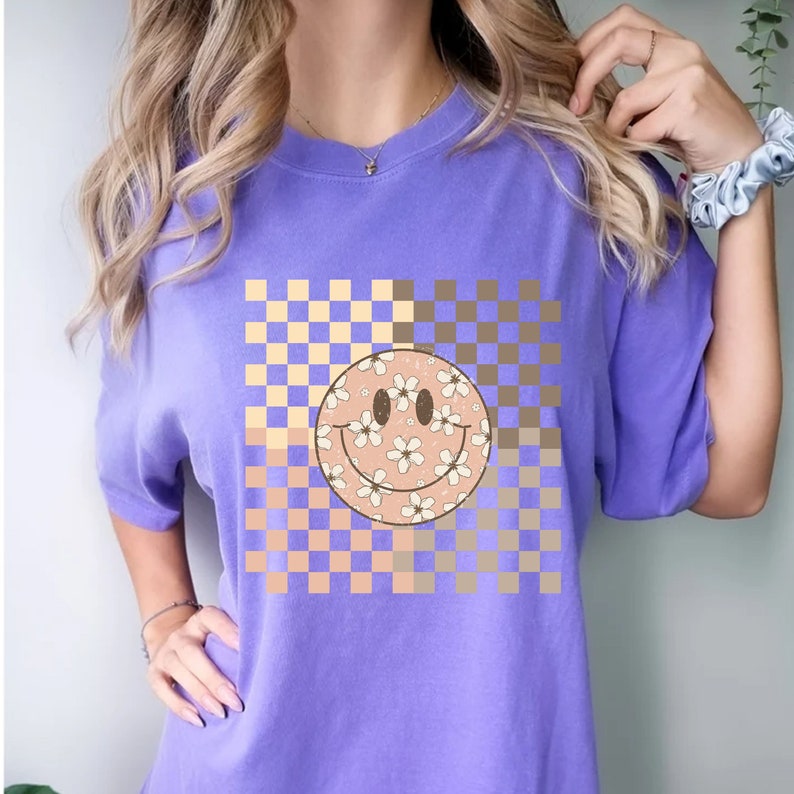Peut inclure: T-shirt violet avec un motif &agrave; carreaux et un smiley floral.