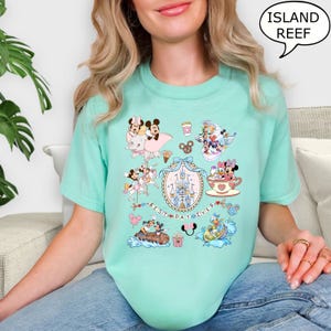 Puede incluir: Camiseta de color verde azulado claro con un gr&aacute;fico colorido de personajes de dibujos animados, incluyendo Mickey y Minnie Mouse, con el texto "BEST DAY EVER". La camiseta tambi&eacute;n tiene el texto "ISLAND REEF" en un bocadillo.