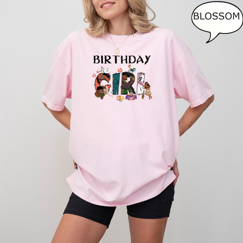 May include: Pink t-shirt with the text "Birthday Girl" in black letters. The letters are decorated with colourful cartoon characters.