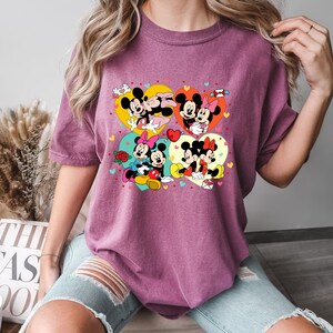 Puede incluir: Una camiseta morada con un estampado gr&aacute;fico de Mickey Mouse y Minnie Mouse en varias poses. El gr&aacute;fico presenta corazones y otros s&iacute;mbolos rom&aacute;nticos.