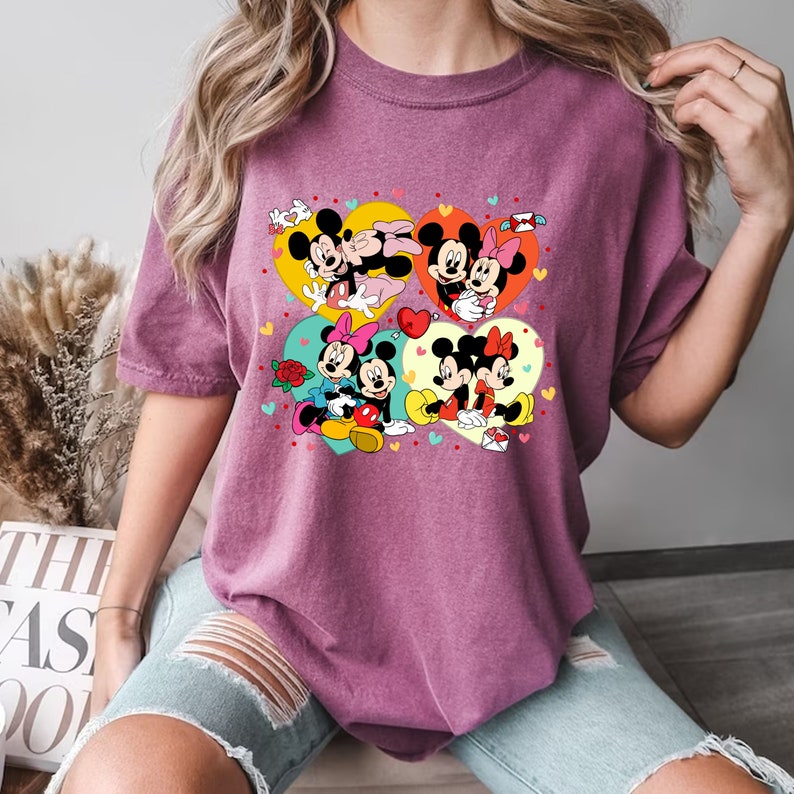 Puede incluir: Una camiseta morada con un estampado gr&aacute;fico de Mickey Mouse y Minnie Mouse en varias poses. El gr&aacute;fico presenta corazones y otros s&iacute;mbolos rom&aacute;nticos.