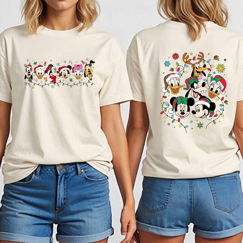 May include: Off-white t-shirts featuring a festive Disney character design. The front of the shirt displays a line of characters with Christmas lights, while the back showcases a larger group of characters with holiday decorations.