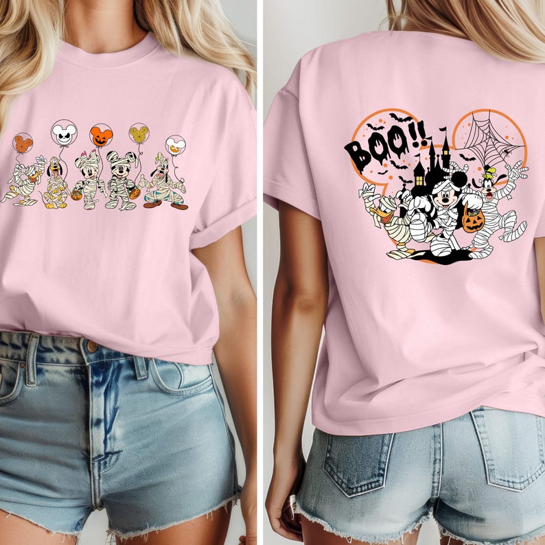 Puede incluir: Camiseta rosa claro con un dise&ntilde;o de Halloween. La parte delantera muestra personajes de dibujos animados momificados sosteniendo globos. La parte trasera tiene la palabra "Boo!!" y m&aacute;s personajes en un dise&ntilde;o circular. La camiseta es de material suave.