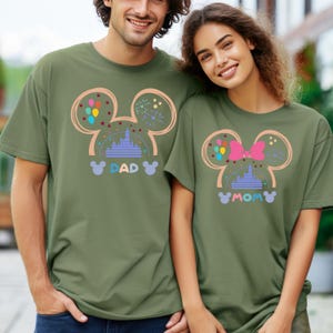 Pode incluir: Duas camisas verdes combinando com um design de cabe&ccedil;a do Mickey Mouse. As camisas apresentam uma imagem de desenho animado do castelo da Cinderela, bal&otilde;es, fogos de artif&iacute;cio e as palavras "DAD" e "MOM".