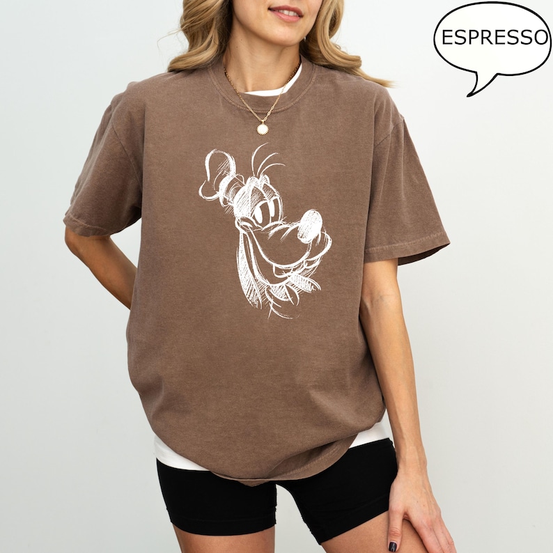 Puede incluir: Una camiseta marr&oacute;n con un dibujo de perro de dibujos animados blanco sonriente. El texto "ESPRESSO" est&aacute; en un bocadillo de di&aacute;logo en la esquina superior derecha de la imagen.