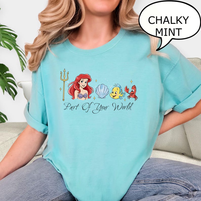 K&ouml;nnte beinhalten: Hellblaues T-Shirt mit hochgekrempelten &Auml;rmeln und einer Grafik von Arielle, einer Muschel, Fabius und Sebastian. Der Text "Part of Your World" steht darunter. Eine Sprechblase sagt "Chalky Mint".