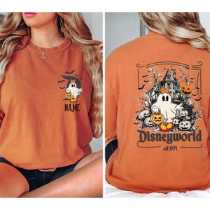 Pu&ograve; includere: Maglietta arancione a maniche lunghe con un design a tema Halloween. La parte anteriore presenta un fantasma dei cartoni animati con una zucca e la parola "NAME". Il retro mostra una scena di casa infestata con "Disneyworld est.1971".