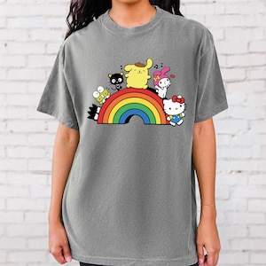 Pode incluir: Uma camiseta cinza com um arco-&iacute;ris e personagens de desenhos animados. Os personagens incluem Hello Kitty, My Melody, Keroppi e um cachorro amarelo.